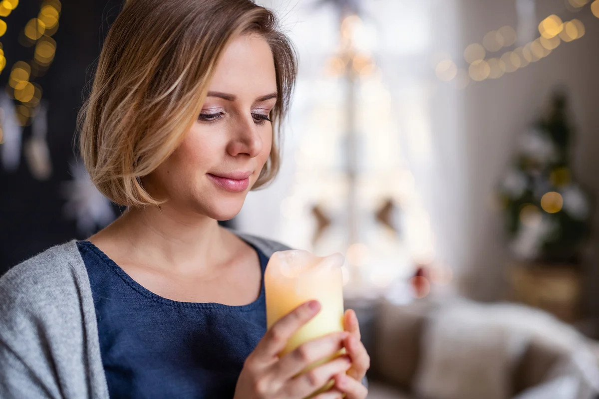 Young woman with candle standing indoors at home at Christmas time