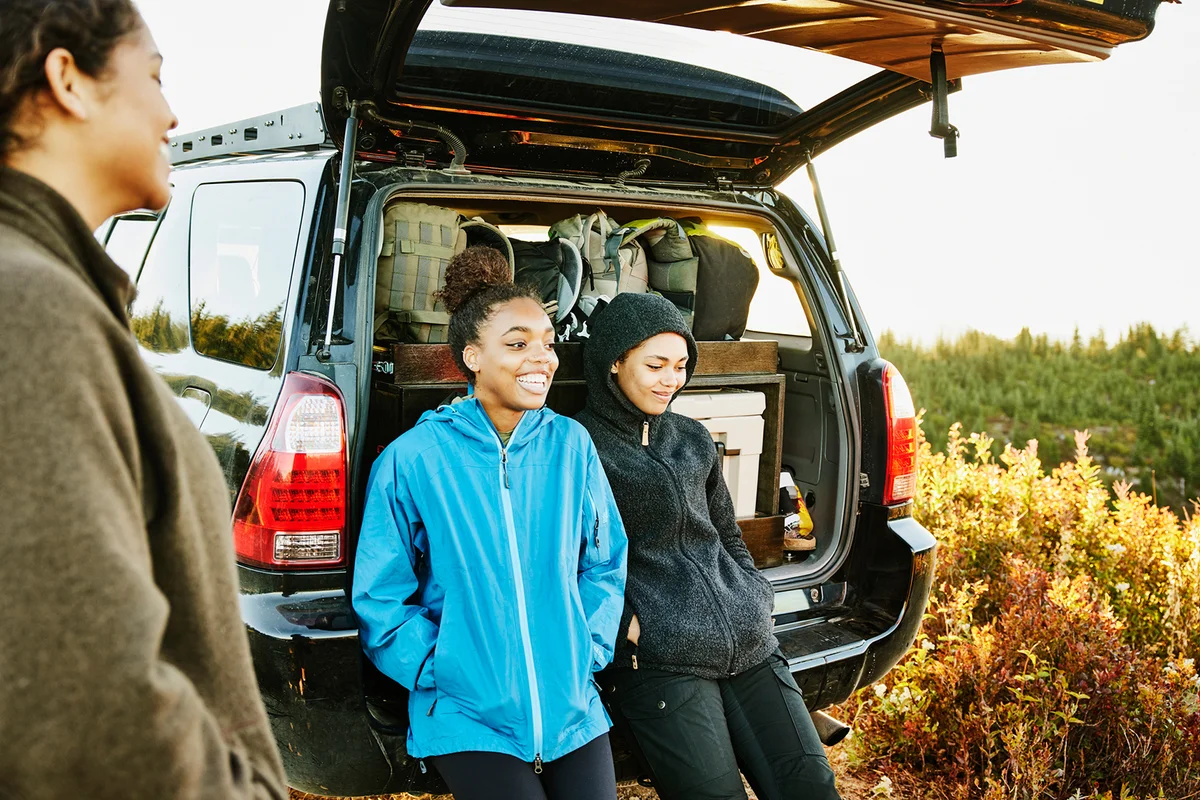 Smiling sisters hanging out at back of car after finishing backpacking trip