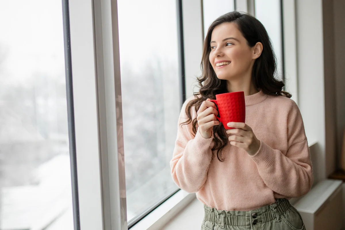 Young woman drinking coffee and day dreaming while looking through window
