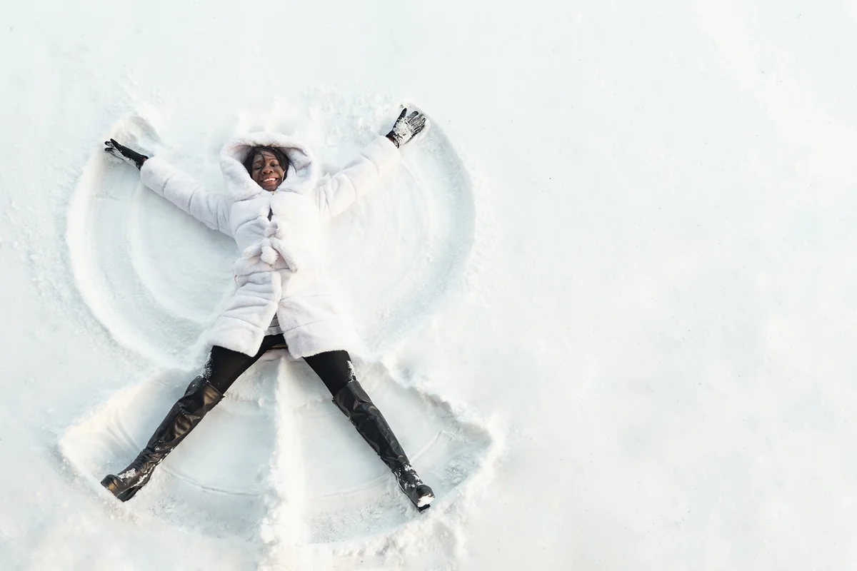 Woman lies on white forest glade and makes snow angles