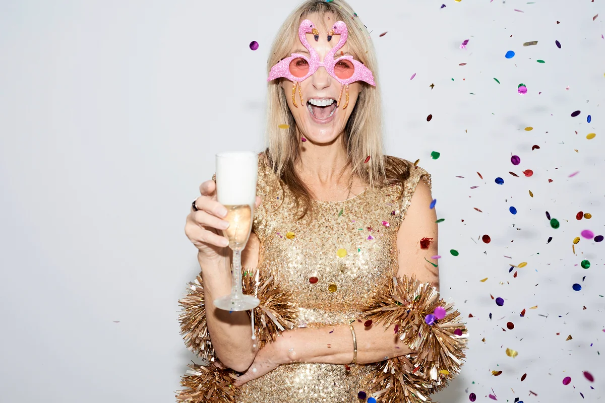 Woman wearing golden dress and flamingo shaped glasses, celebrating New Year's Eve
