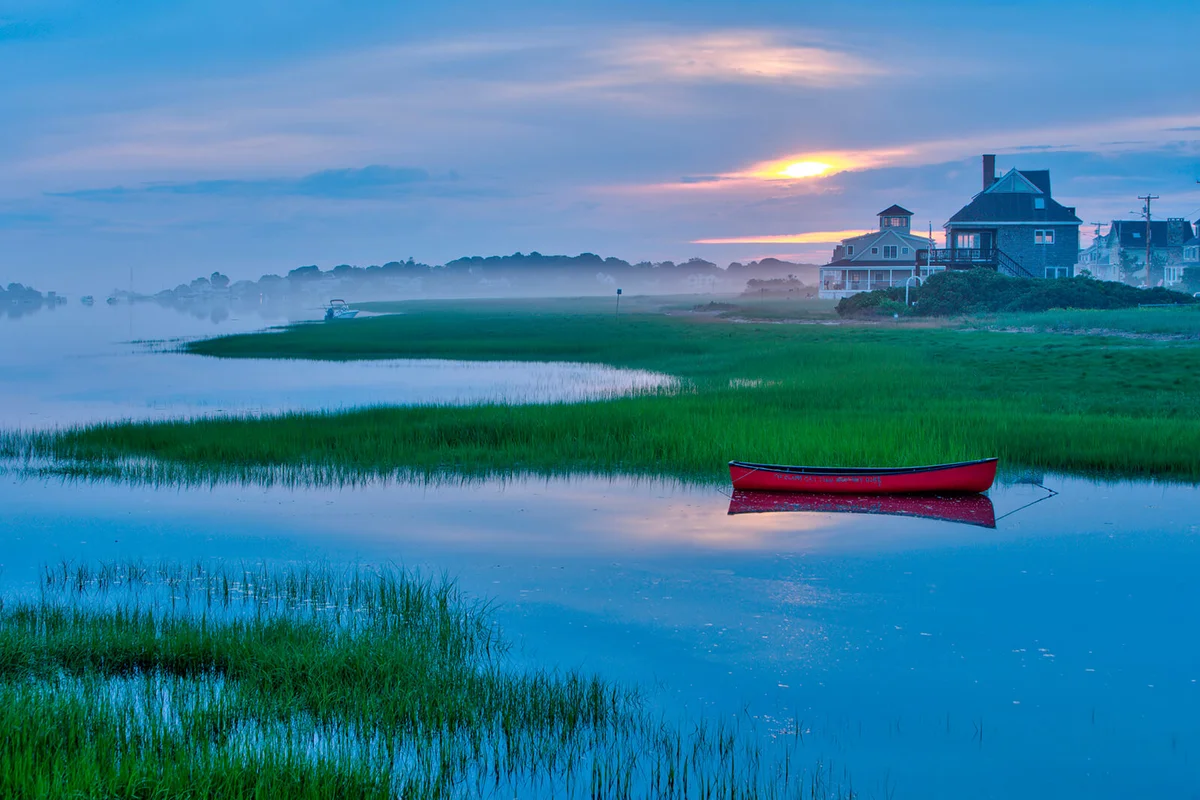 Red canoe floats in Maine Coast tidal inlet after sunset