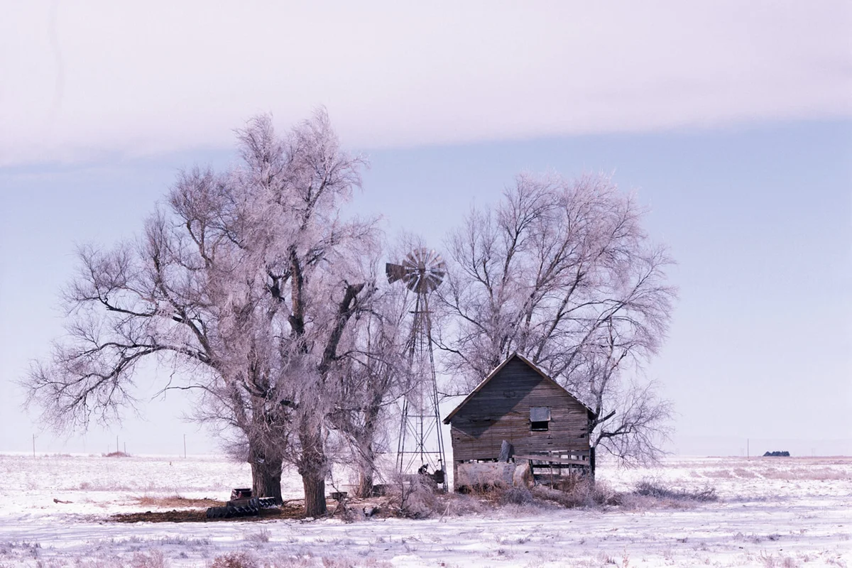 Windmill and abandoned barn in snow covered field