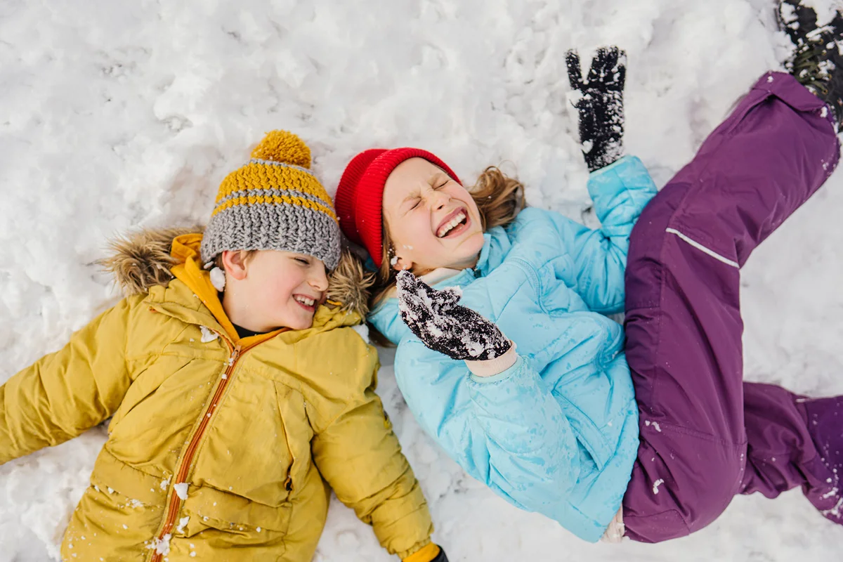smiling girl and boy lying down on snow