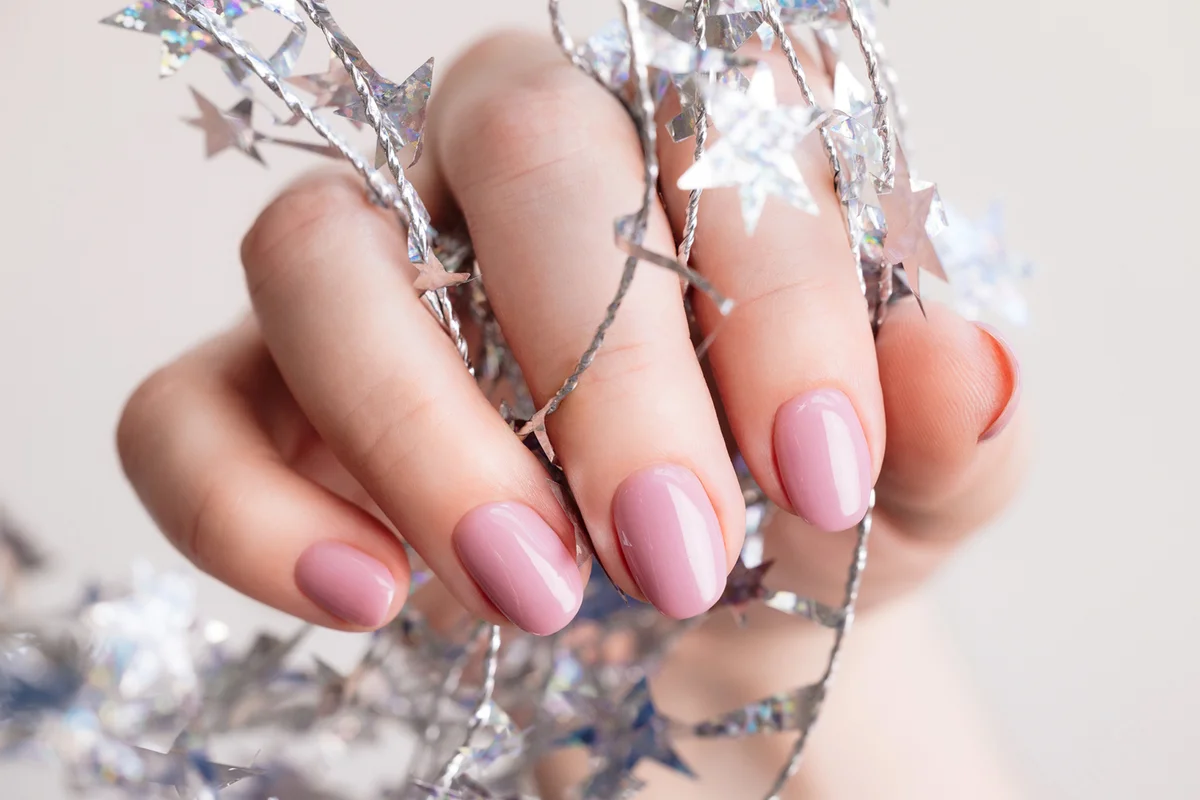Female hand with beautiful holiday manicure - pastel pink gel fingernails with silver twisted wire with stars