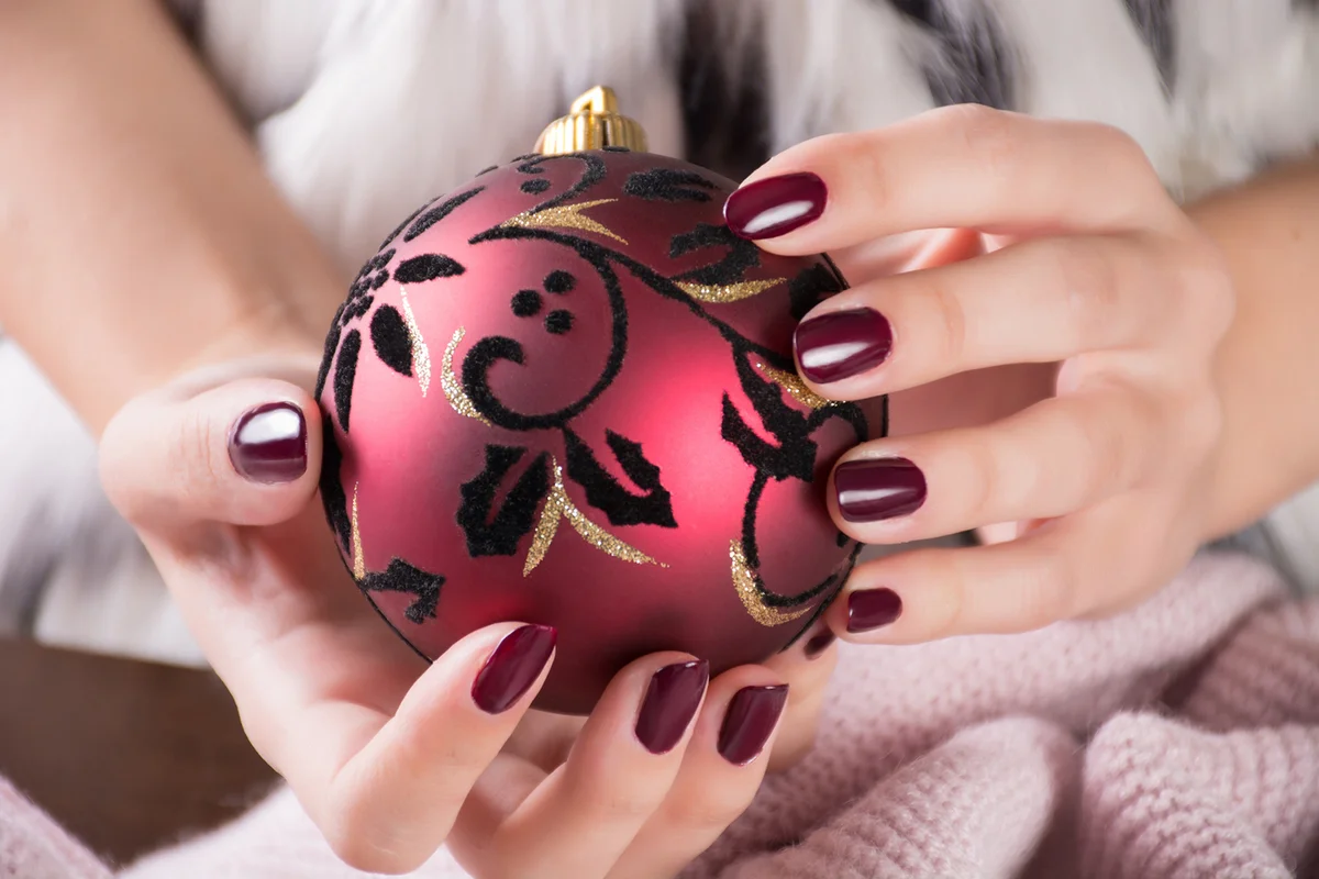 Girl with red wine color nails polish gel and holding Christmas ball