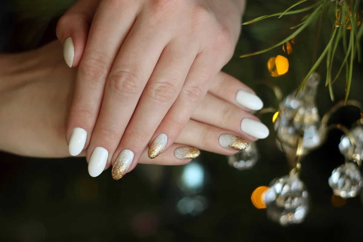 White nails with gold and silver glitter on a background of the Christmas tree