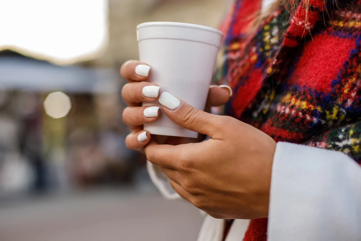 Woman with white nails holding a plastic cup