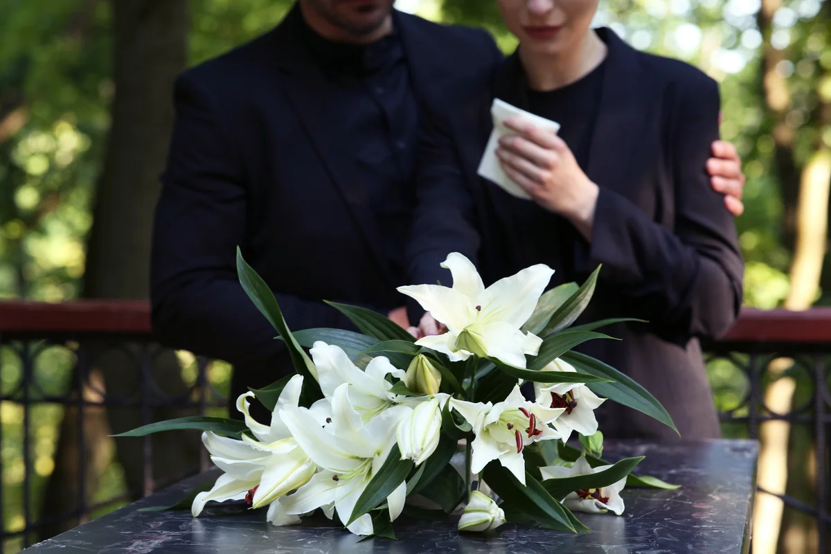 Couple near granite tombstone with white lilies at cemetery