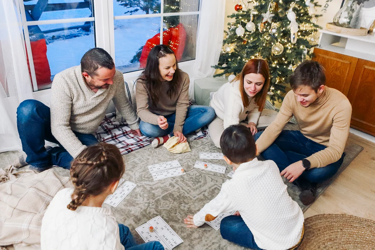 Big family with children sitting on floor near Xmas tree playing lotto board game together
