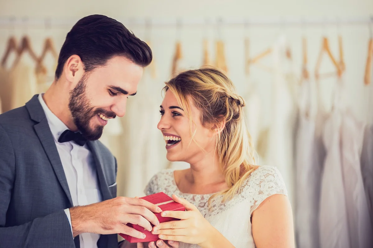 Happy Young Couple Holding Gift While Standing At Bridal Shop