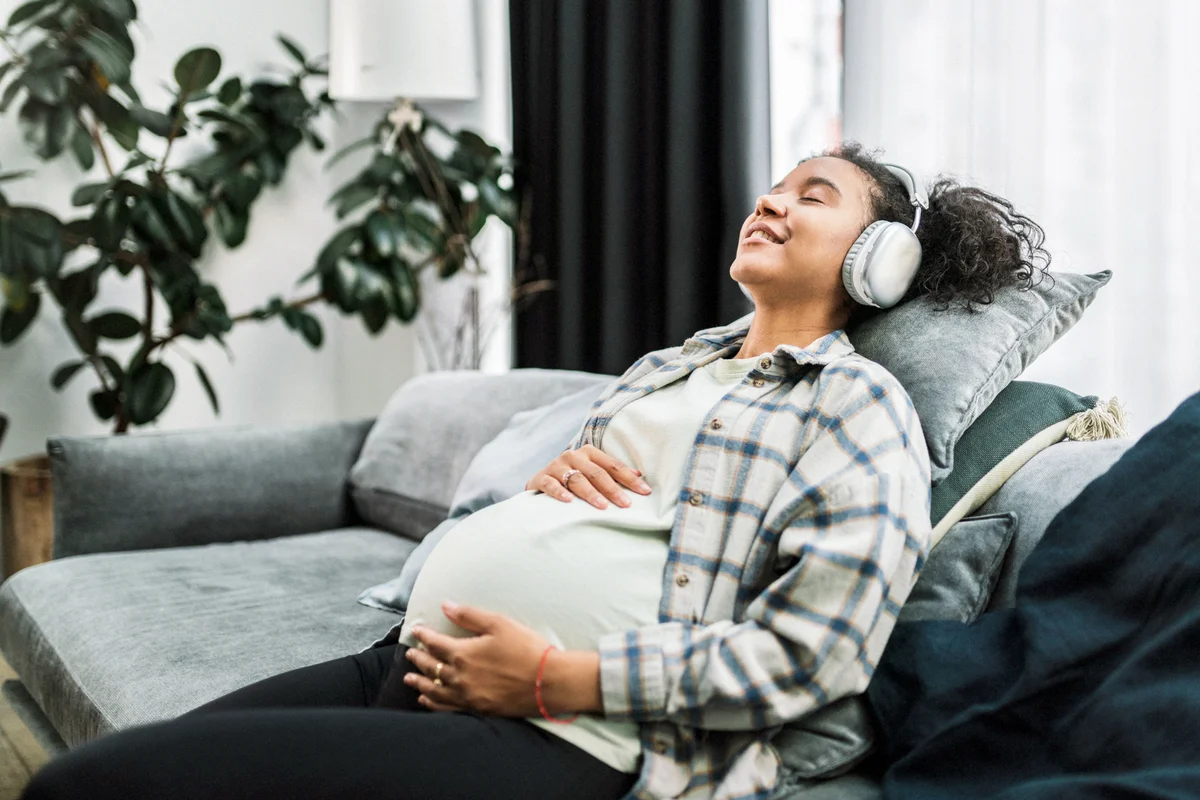 Pregnant woman enjoying music on cozy sofa