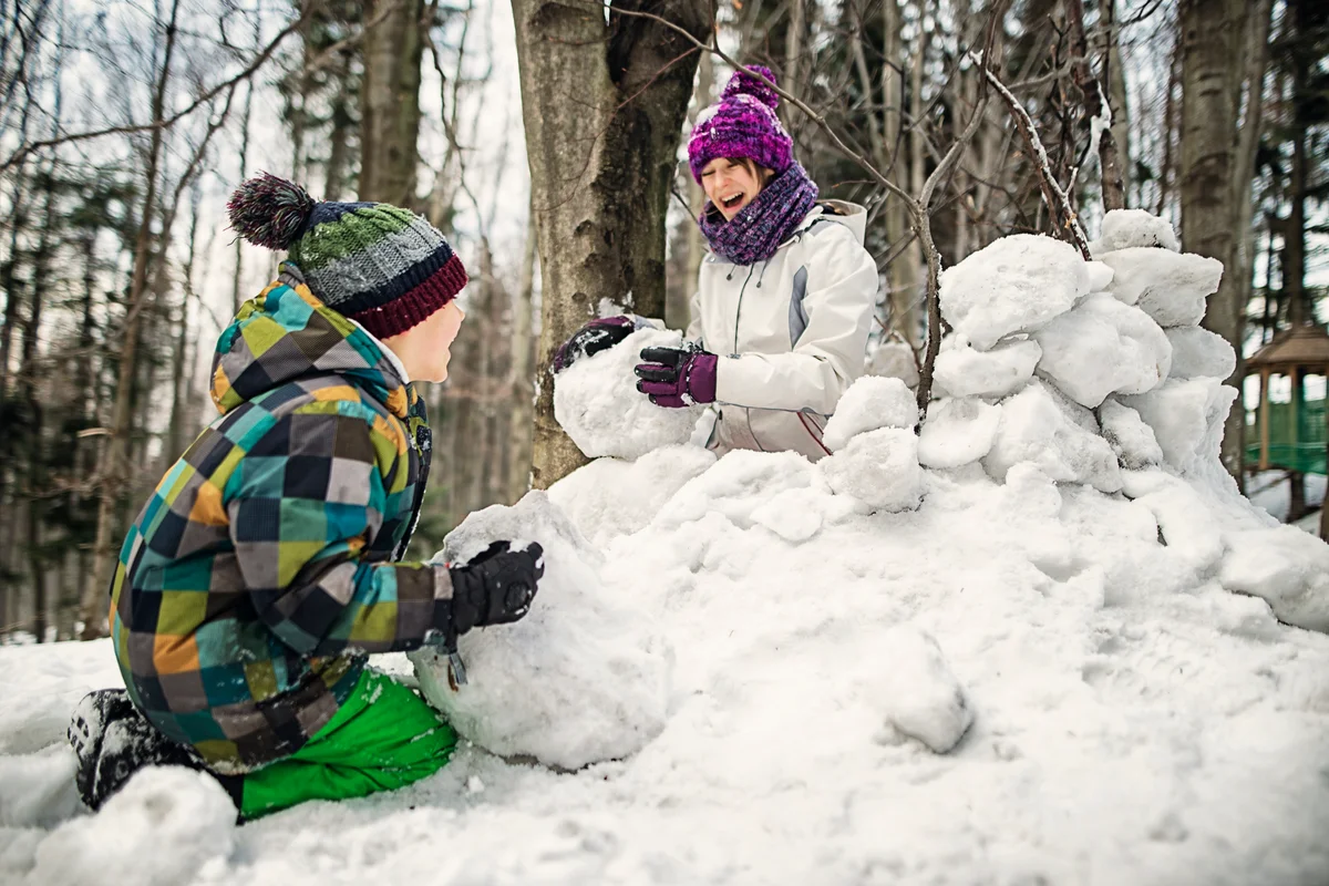 Brother and sister having fun building a snow fortress in forest