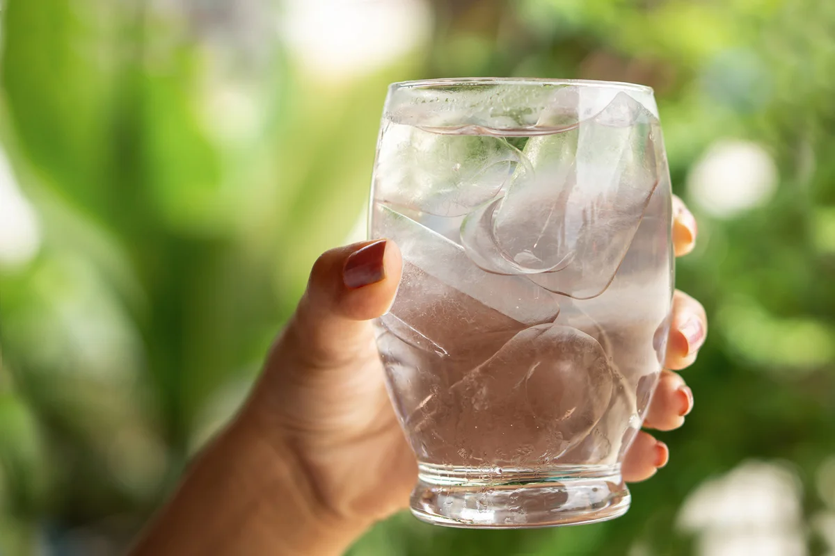 Woman hand holding glass of cold and fresh water with ice