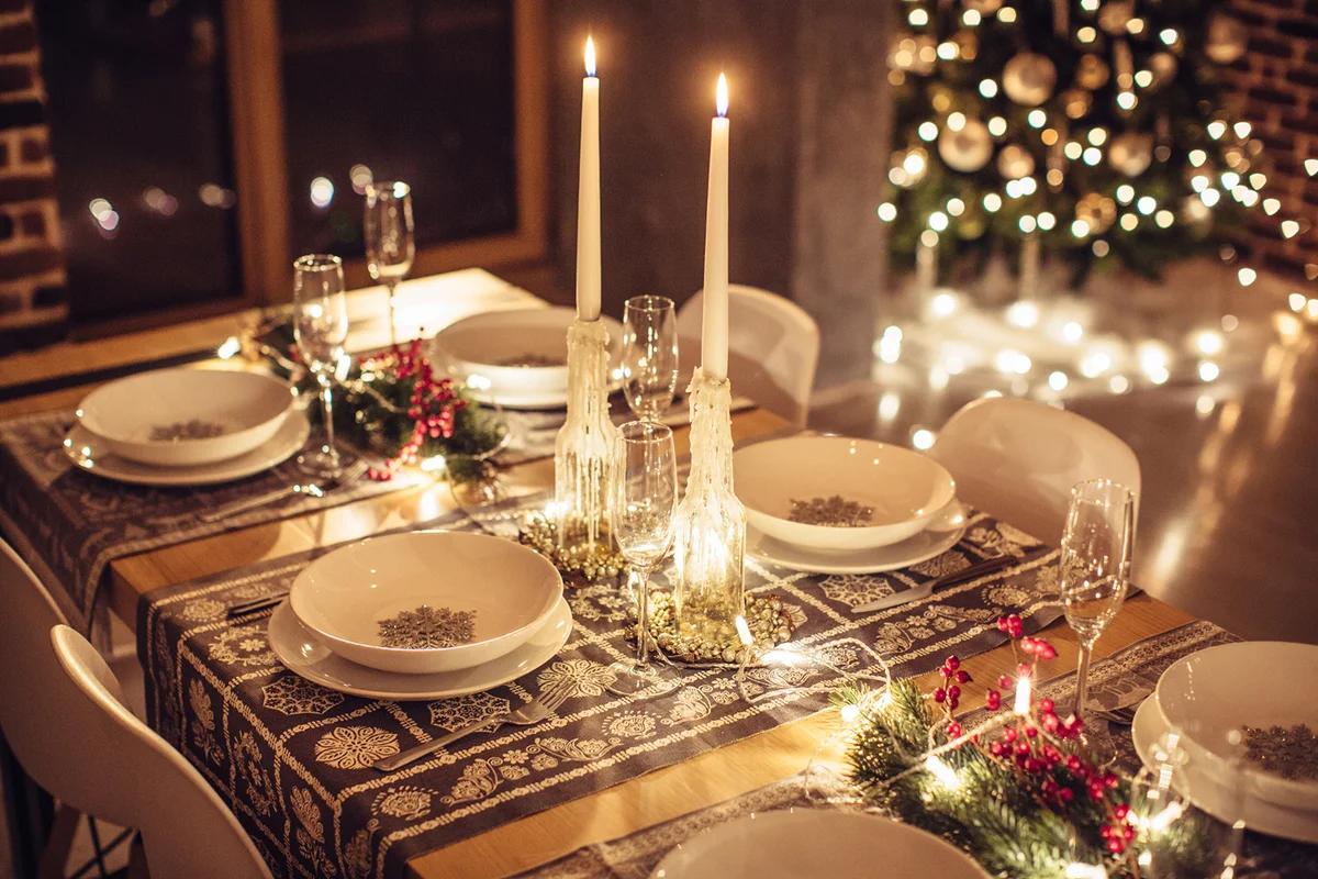 Table set up for Christmas dinner. Evening or night. Christmas tree in background.