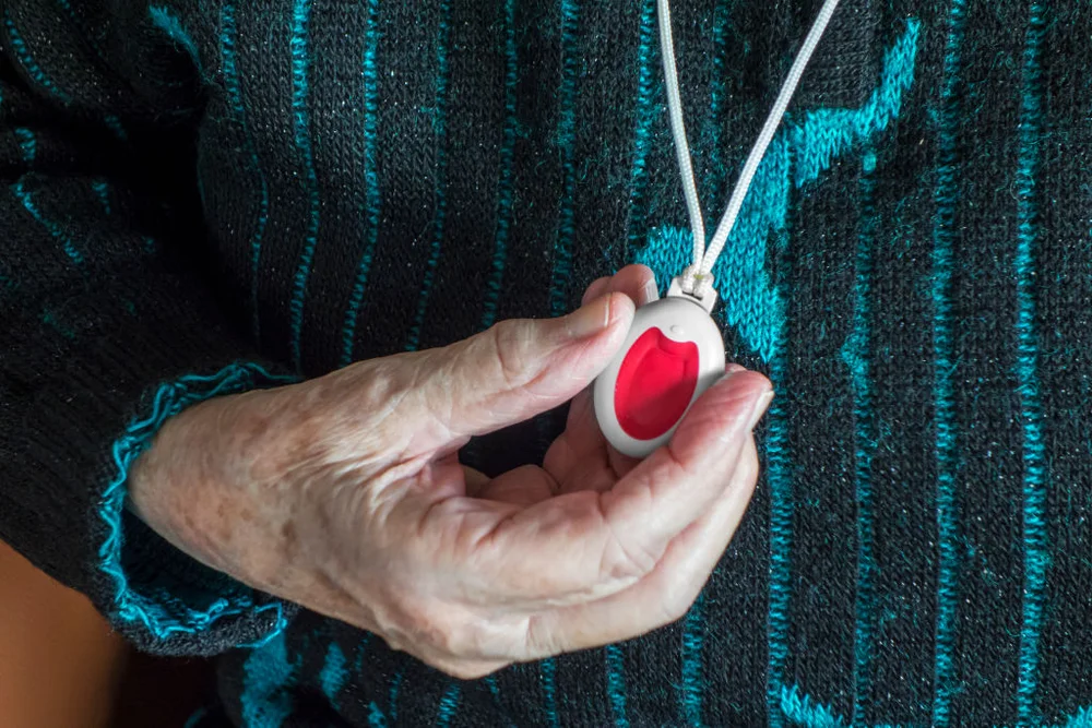 Close up of hand holding life-saving personal alarm for the elderly and disabled people showing pendant with push button.