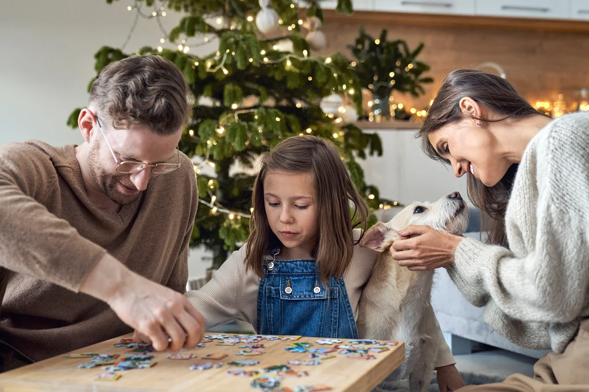 Smiling man and daughter joining puzzle by woman with dog at home