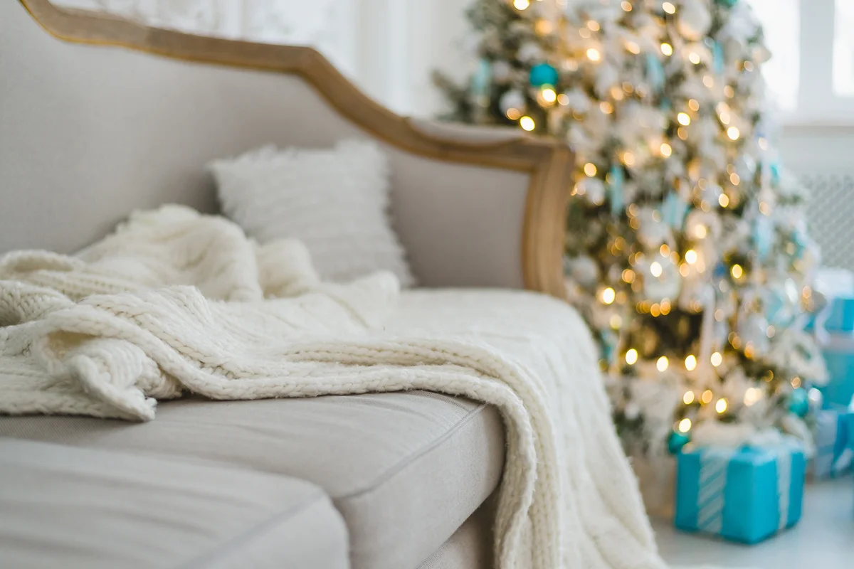 Calm image of blanket on a vintage sofa with tree and gifts