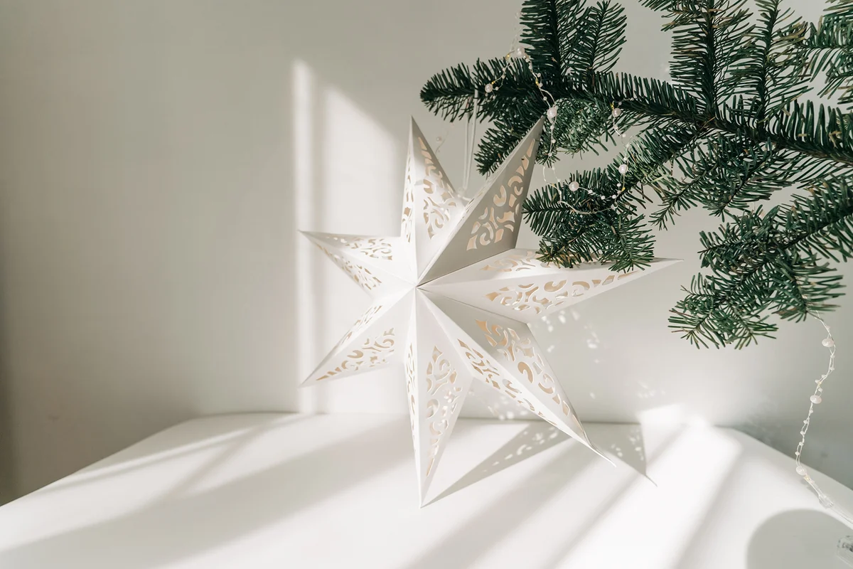 Stylish paper christmas stars hanging on white wall background.