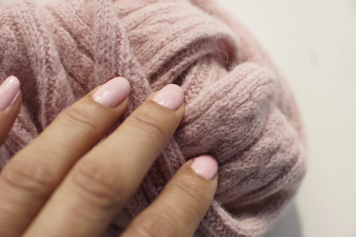 hand with painted pastel pink nail varnish touching a pastel pink knitted wool scarf