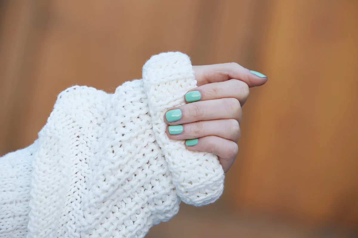 Woman's hands in winter cold clasping knitted sweater with turquoise nail polish