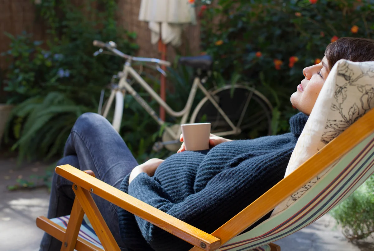 Beautiful pregnant woman relaxing on deck chair with a cup of tea