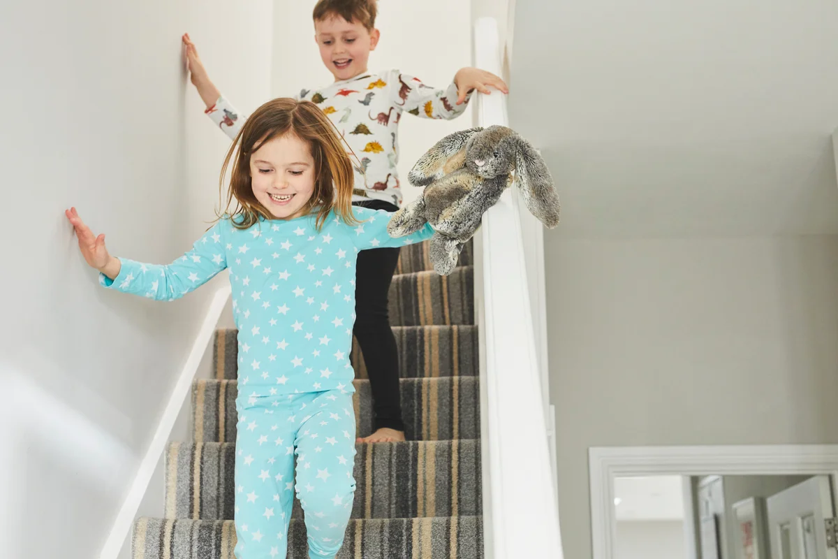 Young boy and girl running down staircase in home wearing pajamas