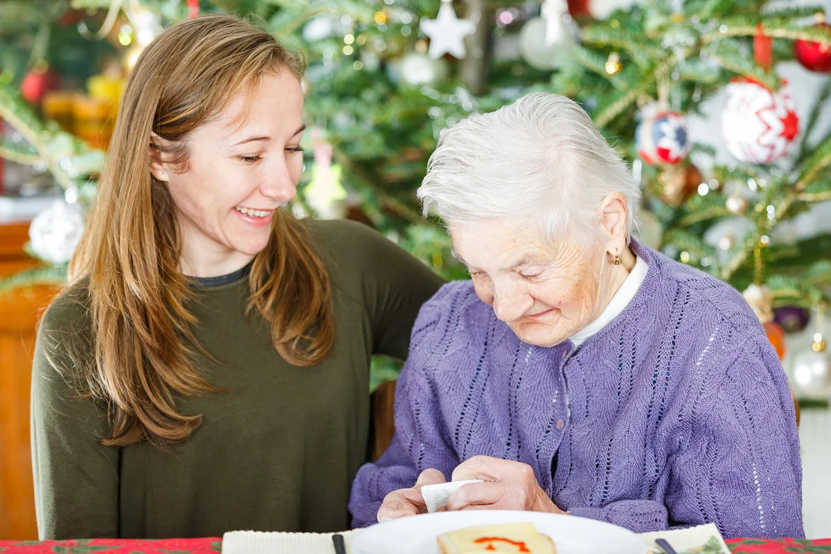 Elderly woman and young carer by Christmas tree