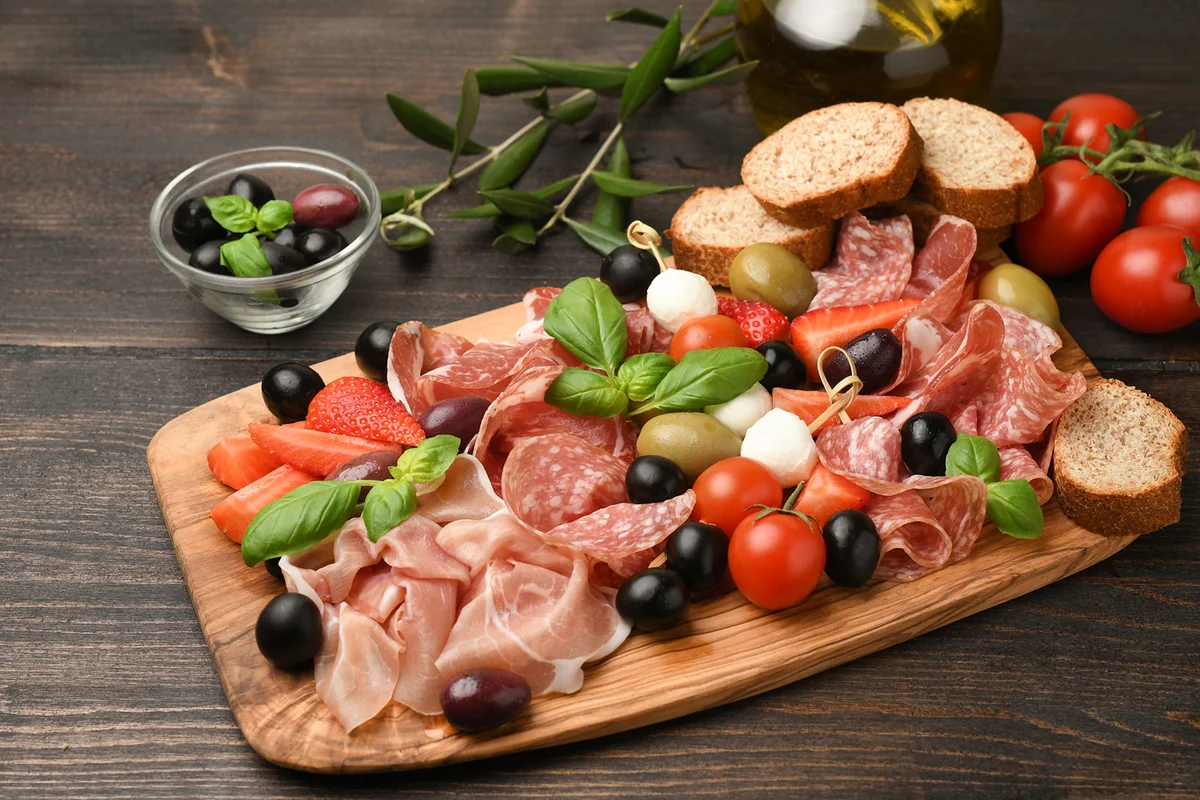 Charcuterie board salami, prosciutto, with green and black olives, appetizers with mozzarella balls, cherry tomatoes and strawberries
