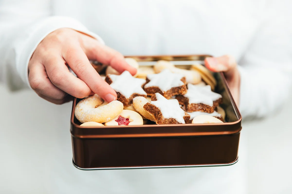 Child hand picking up a christmas cookie from the tin box