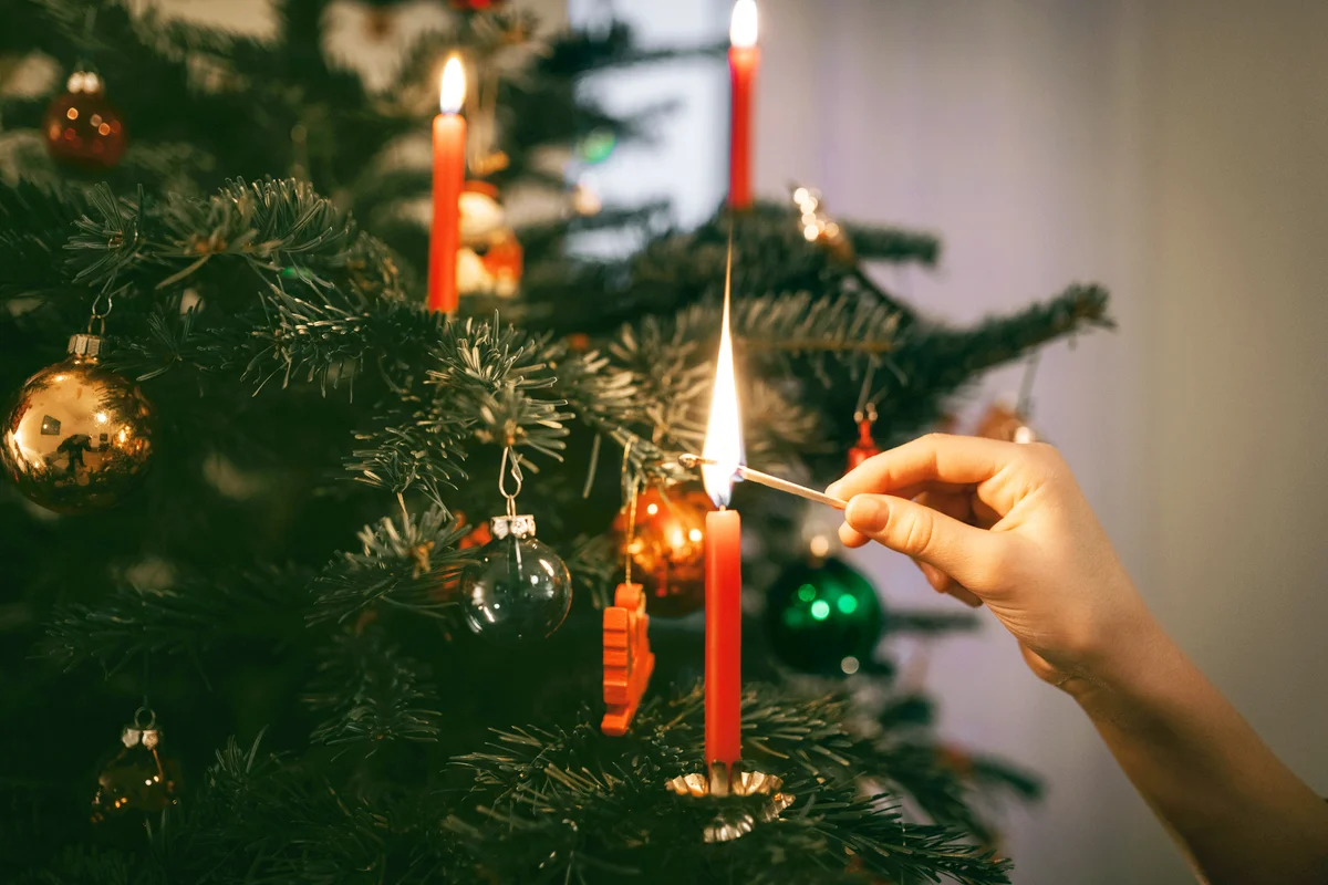 Female hand lighting red candle on christmas tree