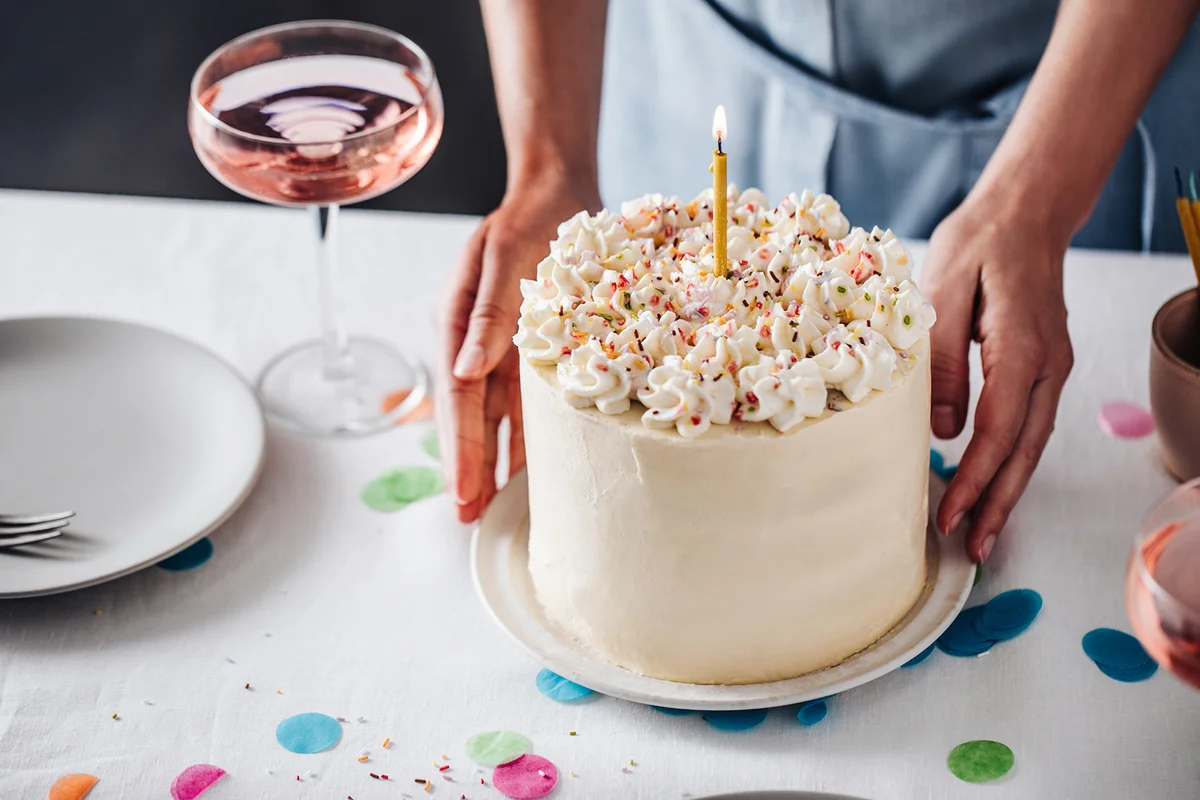 Hands of a female placing birthday cake on table with wine glasses on side.
