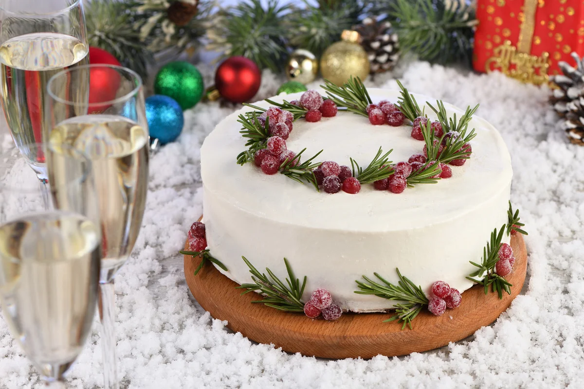 Red Velvet Cake is a traditional red chocolate cake topped with white buttercream and decorated with a Christmas wreath of candied cranberries and rosemary.