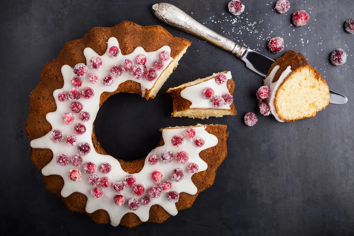 Candied cranberries bundt cake with lemon sugar glaze. Homemade winter holiday dessert on gray background, top view