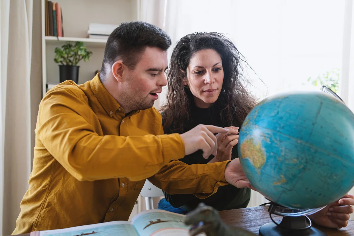 Young man with Down syndrome with his tutor using globe map