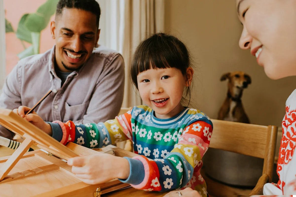 A man and a woman encourage a cute young girl as she draws on an artists easel