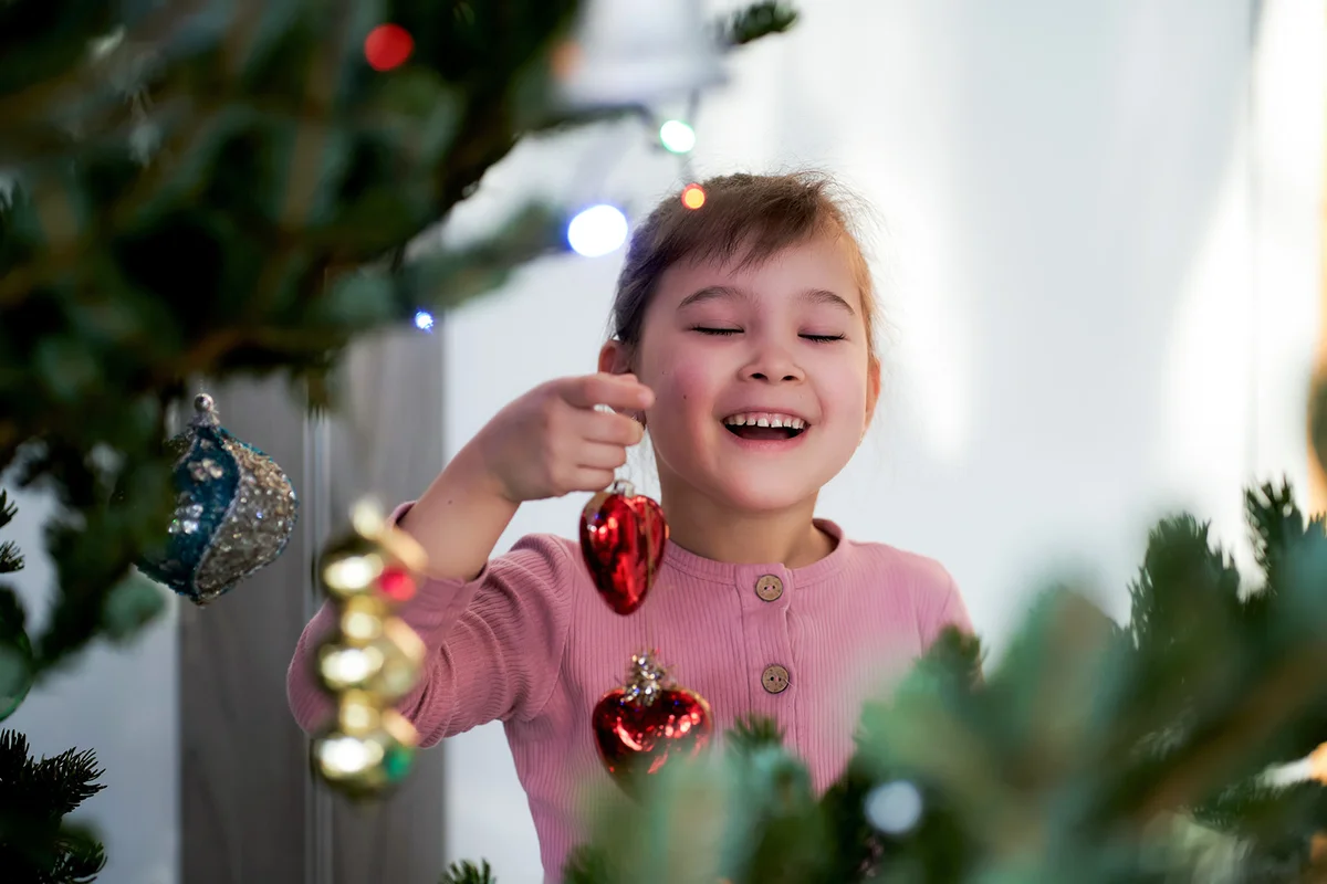 A girl hangs a Christmas toy on a Christmas tree