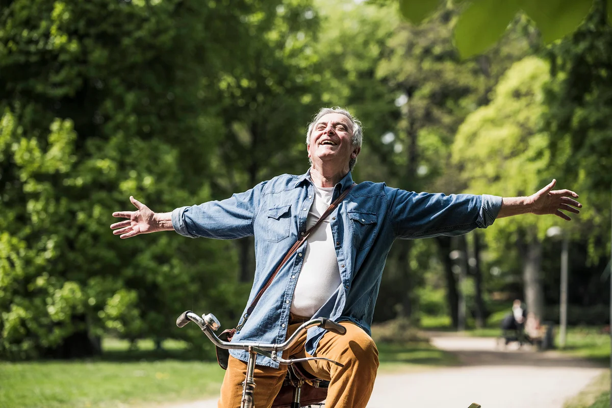 man with arms outstretched riding bicycle at park