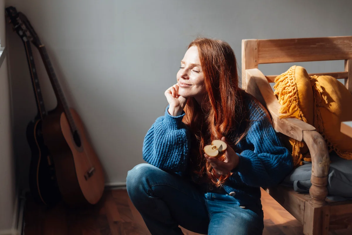 Smiling woman crouching with slice of apple at home