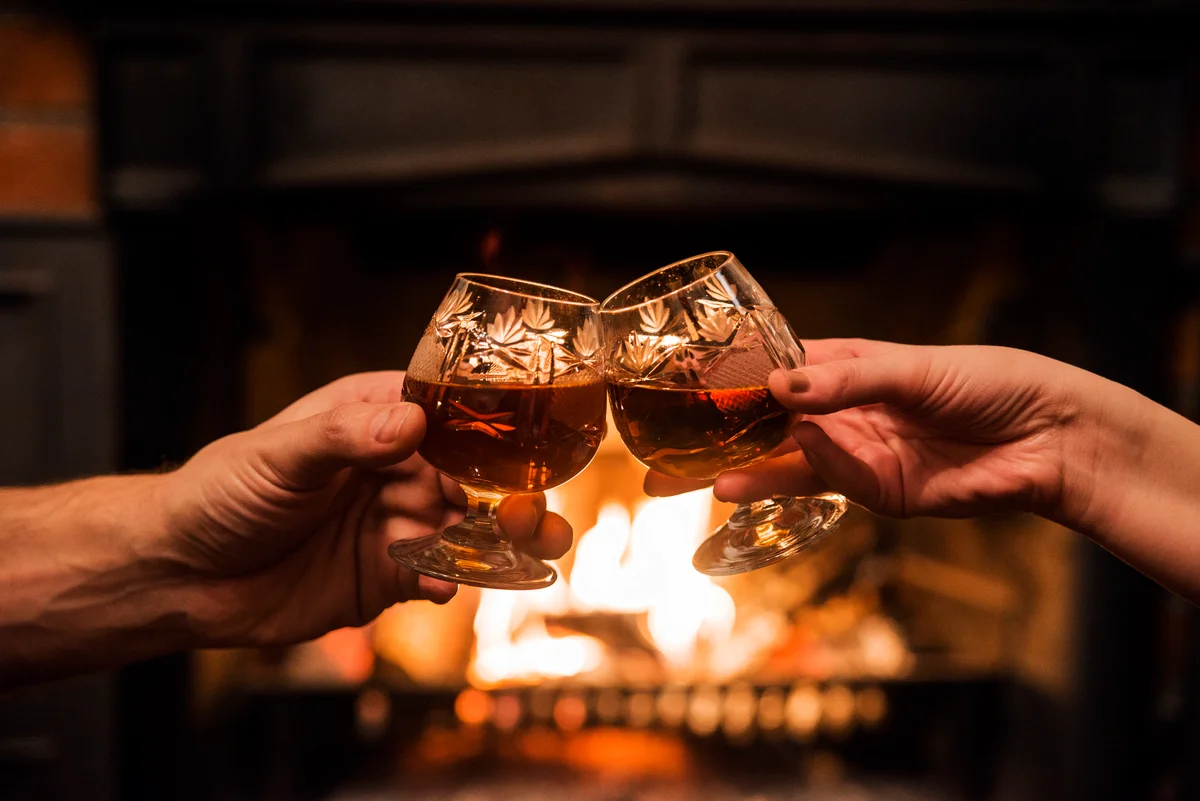 Couple with Two glasses of alcoholic drink in front warm fireplace