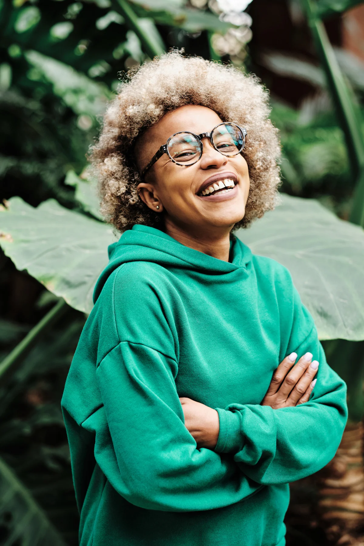 woman laughing while standing with her arms crossed on a green natural background