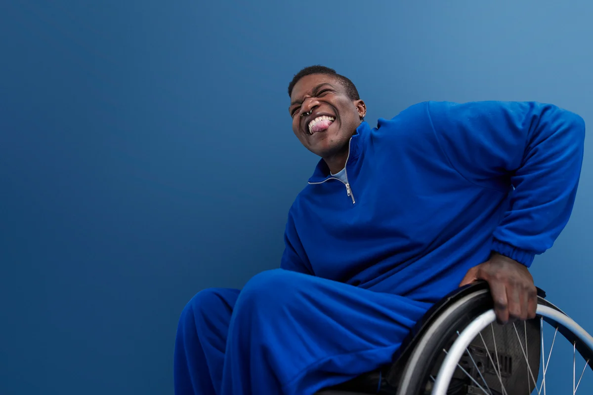 man sticking out tongue while sitting in wheelchair against blue background