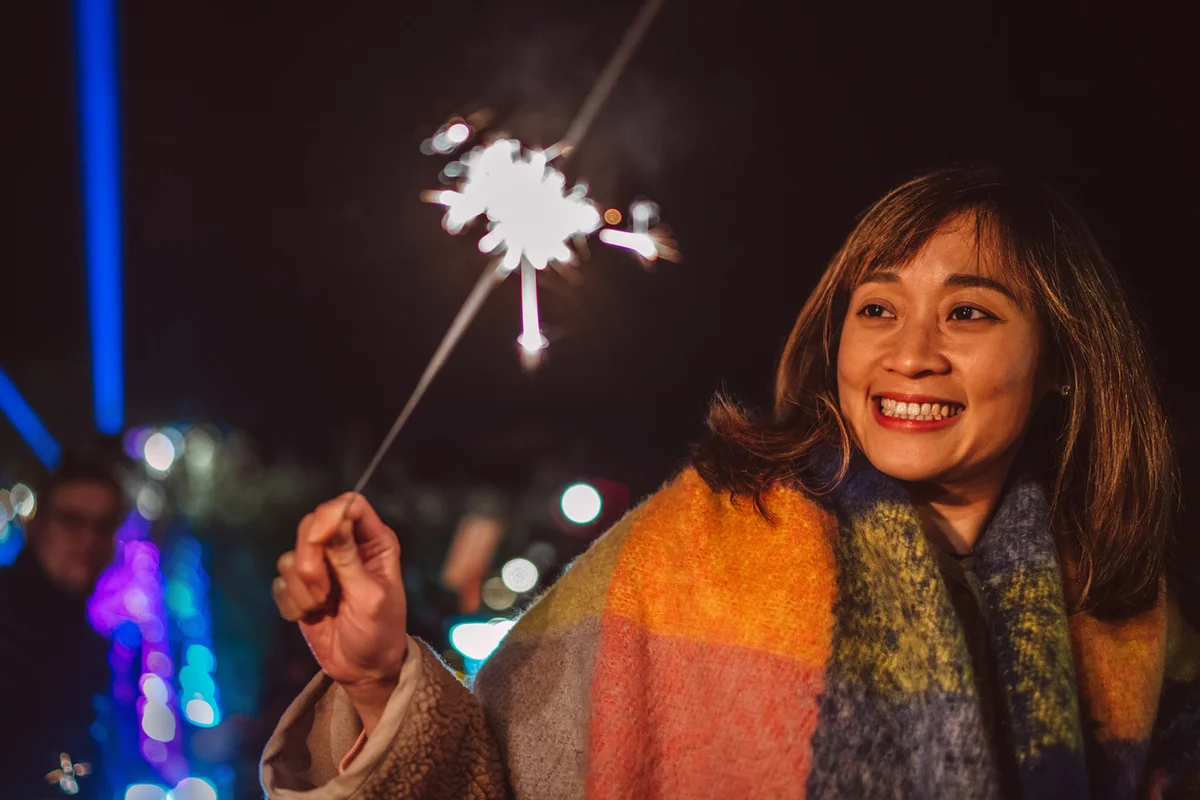 Young cheerful Asian woman holding a lit sprinkler joyfully in carnival at night