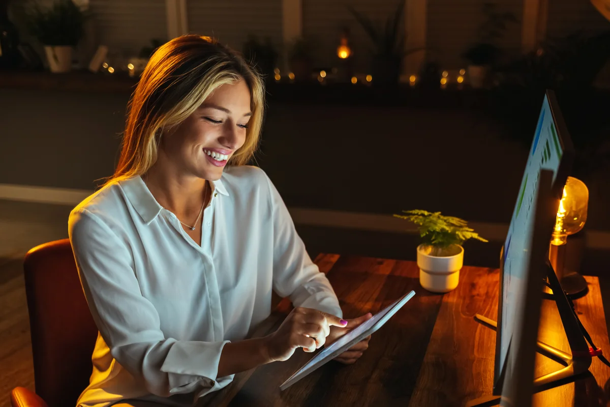 A woman reads on a digital tablet at night at home and laughs