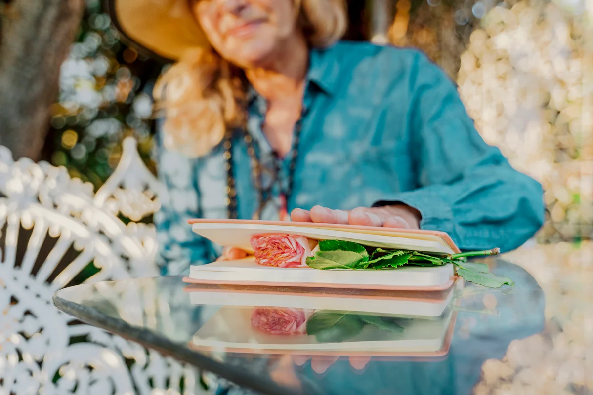 Senior woman pressing rose blossom between book pages