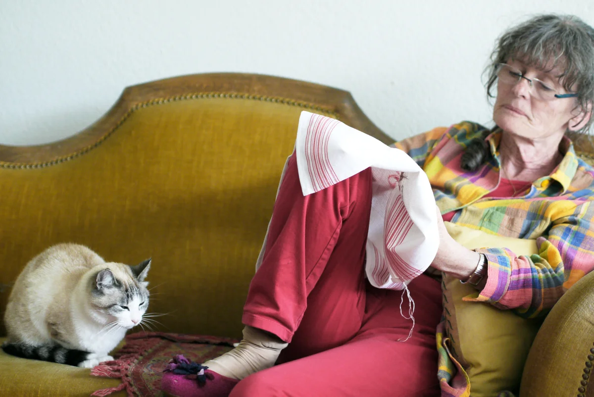 Senior woman doing embroidery on sofa with cat