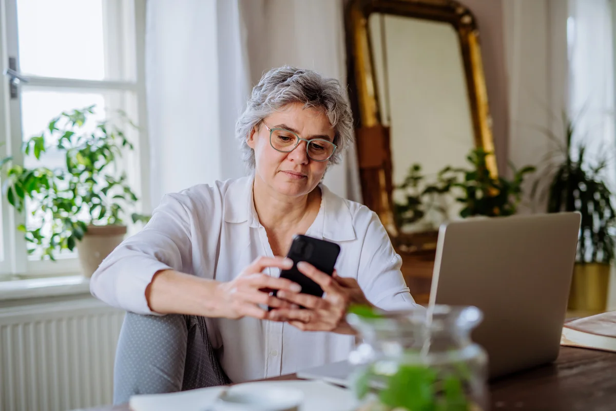 Mature woman using laptop and smartphone at home