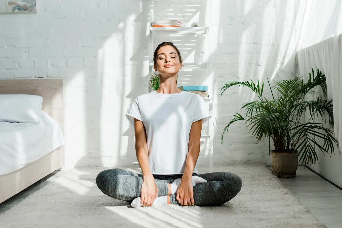 Beautiful happy girl with closed eyes practicing yoga in lotus position in bedroom in the morning