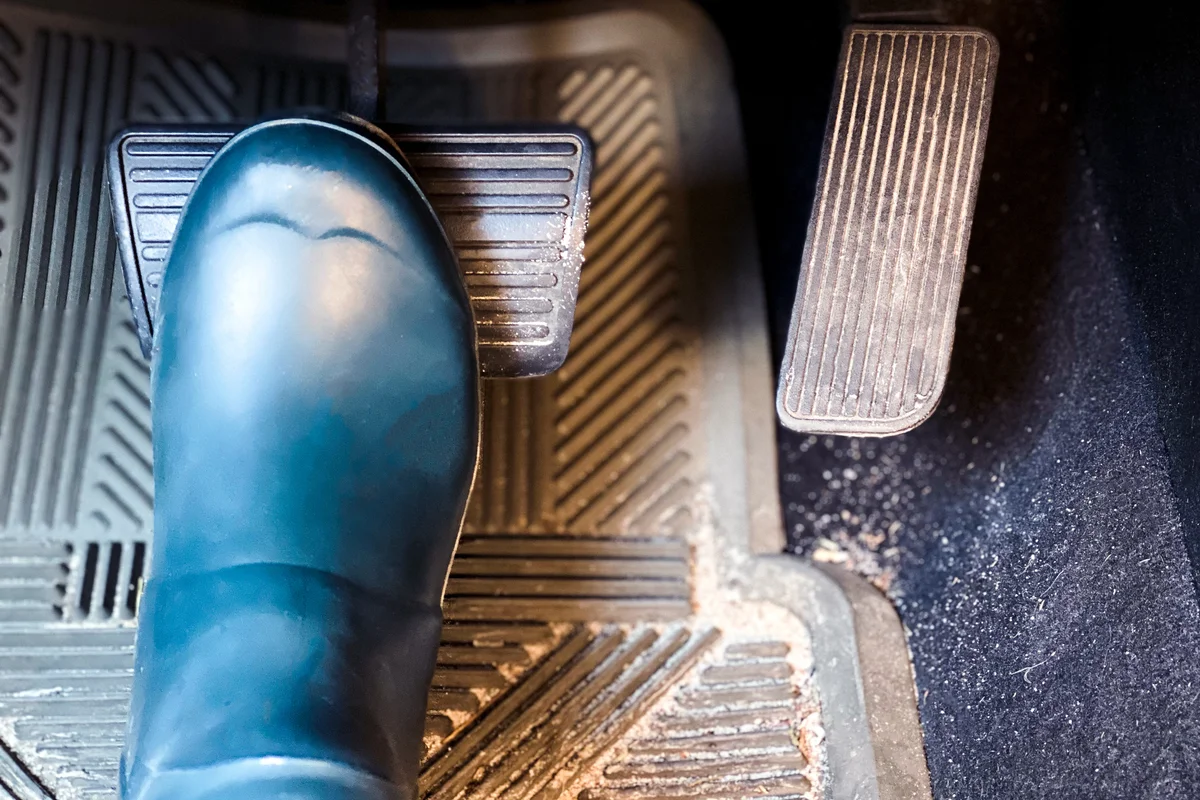 Woman wearing rubber boots has foot on brake while driving car