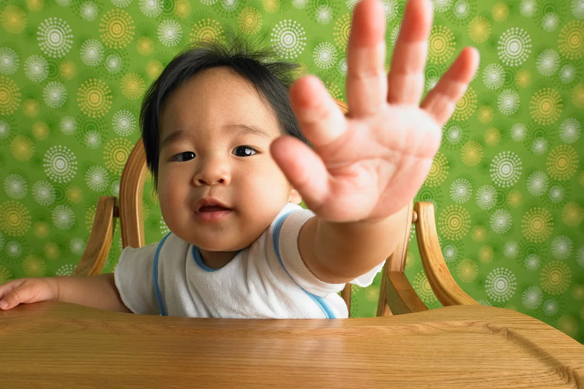 Baby boy (9-12 months) sitting in highchair, arm outstretched